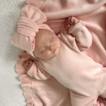 Newborn baby in a pink outfit lying on a white blanket