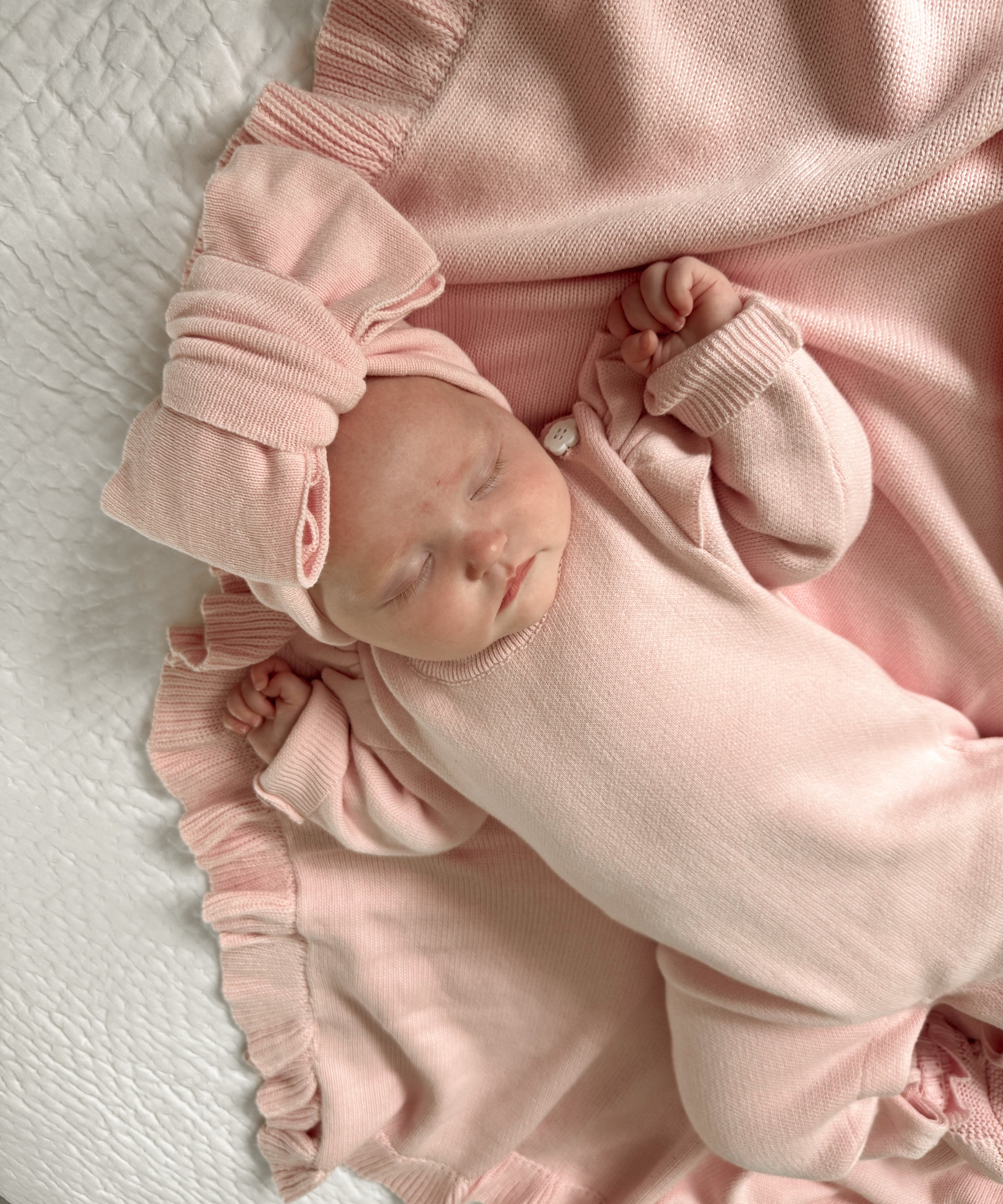 Newborn baby in a pink outfit lying on a white blanket