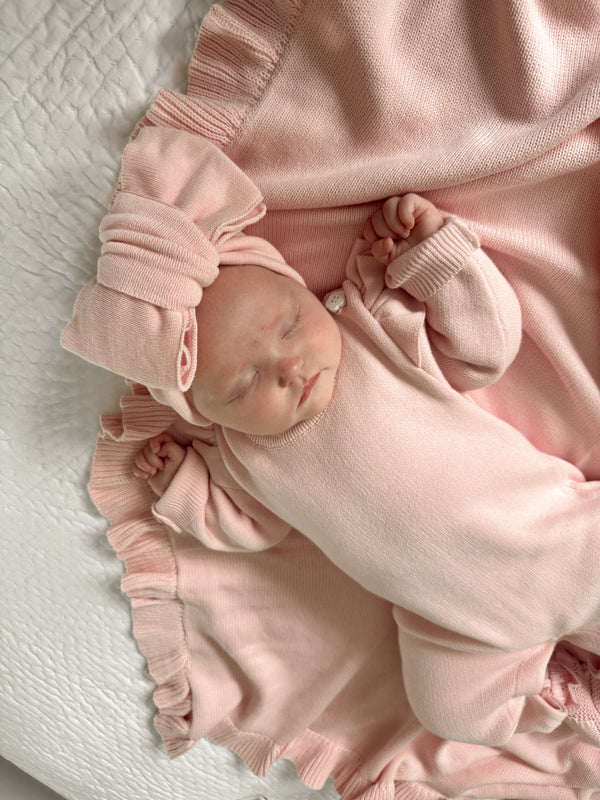 Newborn baby in a pink outfit lying on a white blanket